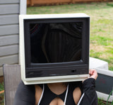 woman wearing a black outfit with cut-out design, standing outdoors with monitor head