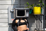 woman wearing a black outfit with cut-out design, standing outdoors with TV head