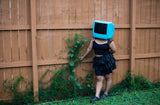 Photo of goth woman wearing turquoise TV head next to flowers